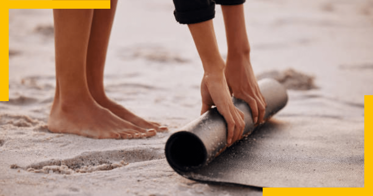 A woman folding her yoga mat on a beach